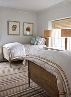 two twin beds in a bedroom with white walls and carpeted flooring next to windows