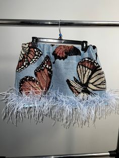 a purse hanging on a metal rack with white feathers and butterflies printed on the fabric