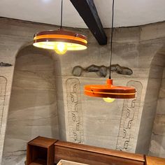 two lamps hanging from the ceiling in a room with stone walls and wooden furniture on either side