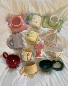 there are many different cups and saucers on the white bed sheet, one is empty