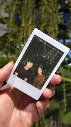 a person holding up a polaroid in front of some plants