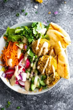 a white bowl filled with salad and fries on top of a gray table next to condiments