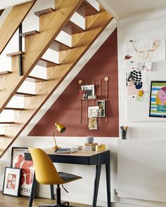 a desk with a chair under a stair case next to a wall mounted art piece