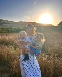 a woman holding two small children in a field