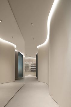 an empty hallway with white walls and lights on the ceiling is lit by recessed lighting