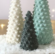 three crocheted christmas trees sitting on top of a white fluffy rug next to each other