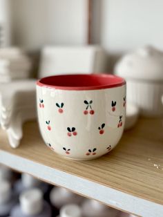 a red and white bowl sitting on top of a wooden shelf next to other bowls