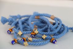 several bracelets with gold crosses and evil eyes on blue cords, all decorated with beads