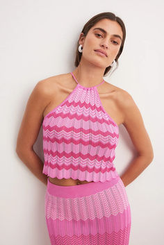 a woman in a pink dress leaning against a wall with her hands on her hips