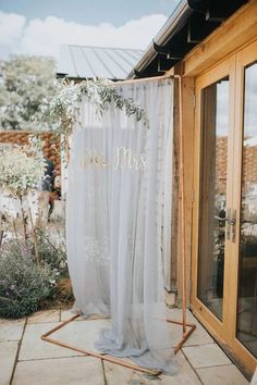 an outdoor wedding ceremony with white drapes and greenery on the side of the building