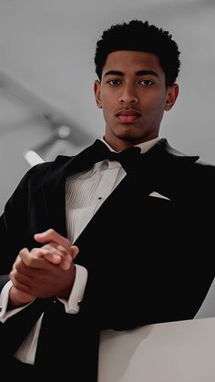 a young man in a tuxedo poses for the camera with his arms crossed