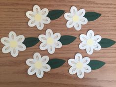 six paper flowers with green leaves on a wooden surface, cut out to look like they have been placed together