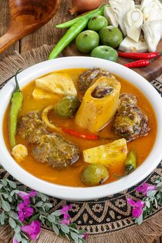 a white bowl filled with food on top of a wooden table next to green peppers