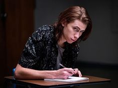 a woman sitting at a table with a pen and paper in front of her face