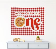 a red and white checkered wall hanging above a dresser with a pizza on it