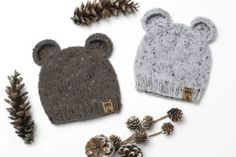 two knitted hats with pine cones, one is grey and the other is gray