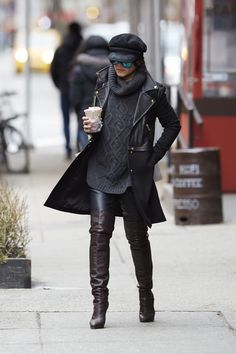 a woman walking down the street while holding a cup of coffee in her hand and wearing knee high boots