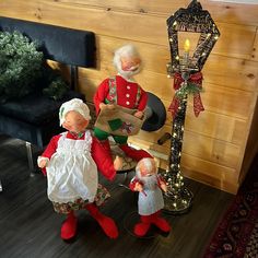 two old fashioned dolls are sitting next to a lamp post and christmas tree with lights on it