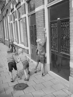 black and white photograph of two boys reaching up to open the front door of a building