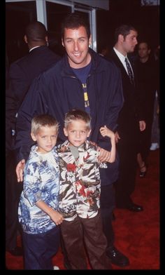 a man standing next to two boys on a red carpet