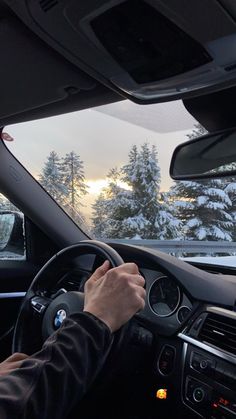 a person driving a car on a snowy road with trees in the background and sun shining through the windshield