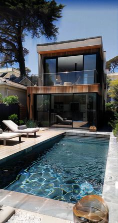 an outdoor swimming pool with lounge chairs around it and a deck in front of the house