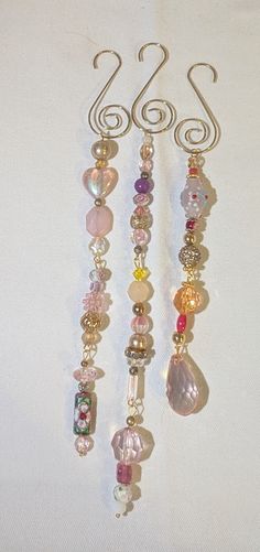 three pieces of glass and metal hanging on a white surface with some beads attached to it