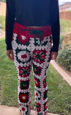 a person standing in the grass wearing red and white crocheted pants