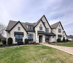 a large white house with black windows and lots of grass in front of it on a cloudy day