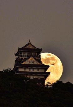 the full moon is seen behind an old building on top of a hill in japan