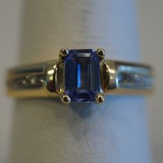 an engagement ring with a blue sapphire and two diamonds on the side, set in yellow gold