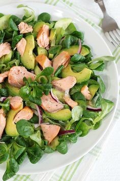 a salad with salmon and spinach on a plate next to a knife and fork