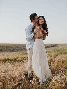 a man and woman are hugging in the middle of an open field with tall grass