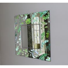 there is a mirror with green leaves on it and a lamp in the reflection behind it