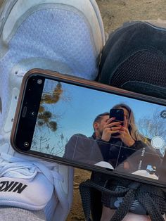 a man taking a selfie with his cell phone while sitting on the ground next to someone's feet