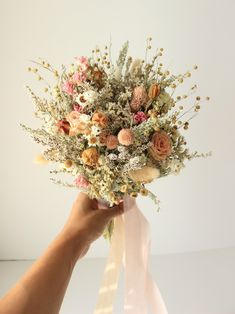 a person holding a bouquet of flowers in their hand on a white surface with a pink ribbon around it