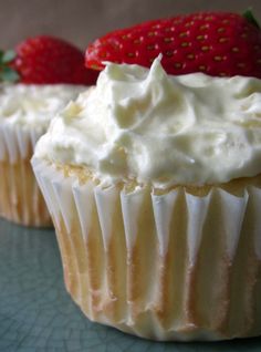 three cupcakes with white frosting and strawberries on top