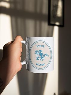 a hand holding a coffee mug with a horse and rider on the inside, in front of a window