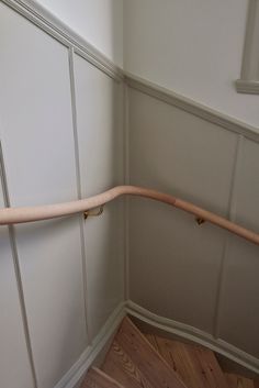 the corner of a room with wood flooring and white walls, along with a wooden hand rail