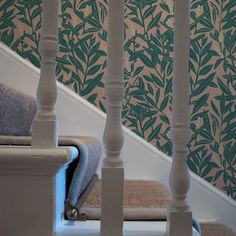 a stair case next to a wallpapered staircase with green leaves on the wall