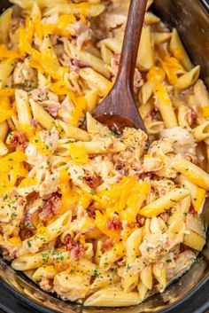 a wooden spoon in a crock pot filled with pasta and chicken salad, garnished with parmesan cheese