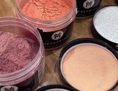 several different types of powders on a wooden table with one being pink and the other is white