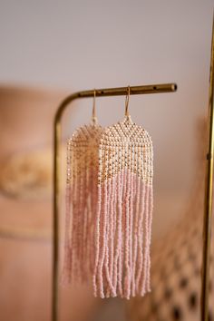 a pair of pink beaded earrings hanging from a metal stand on a table next to a wall