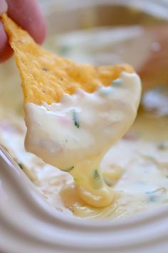 a hand holding a tortilla chip over a bowl of dip