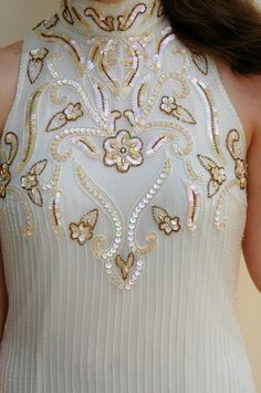 a woman wearing a white dress with gold and silver embellishment on the neck