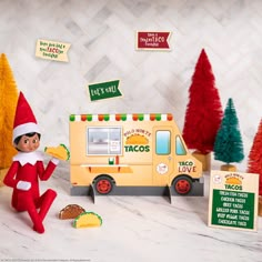 an elf is sitting in front of a taco truck and some christmas tree decorations