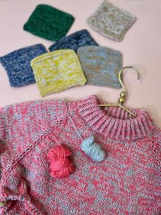 knitted sweaters and crochet hooks laid out on a pink table top