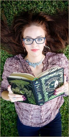 a woman wearing glasses and reading a book in the grass with her hair blowing in the wind