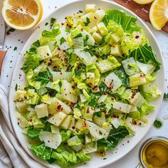 a white plate topped with lettuce salad next to sliced lemons and sauce