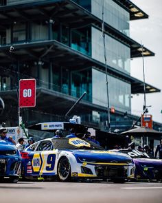 two race cars parked in front of a tall building with people standing around it on the side of the road